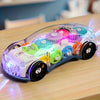 A clear plastic stunt car with colorful gears, lights, and music components resting on a wooden surface.