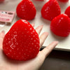 A hand holds a bright red strawberry squishy fidget toy with visible texture and bubbles.