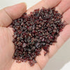 A hand holds a pile of dark reddish-brown natural tumbled stone chips for jewelry making and home decor.