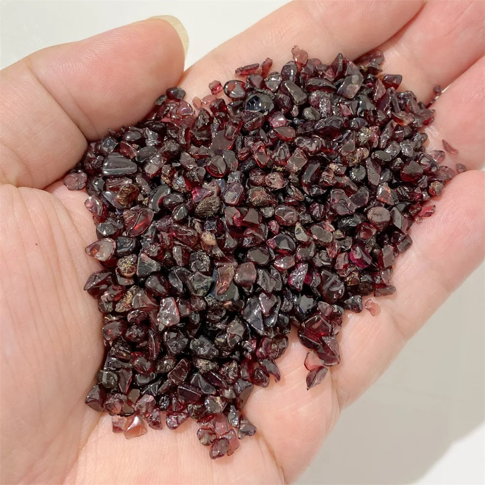 A hand holds a pile of dark reddish-brown natural tumbled stone chips for jewelry making and home decor.