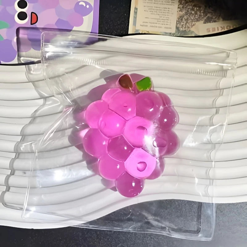 A pink squishy grape fidget toy is placed inside a clear plastic sleeve on a white surface.