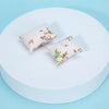 A set of two floral patterned mini pillows displayed on a white circular surface.