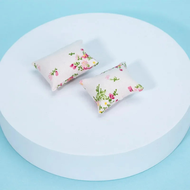 A set of two floral patterned mini pillows displayed on a white circular surface.