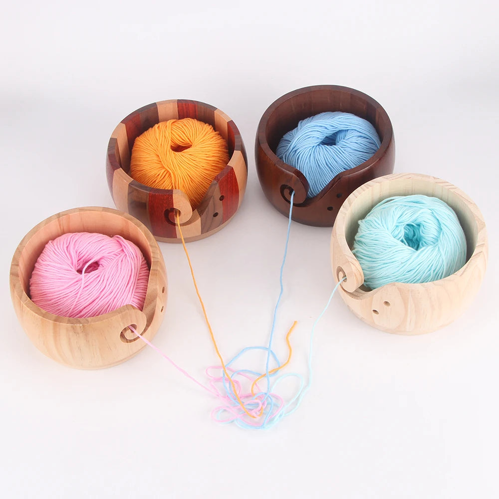 Three wooden yarn bowls containing skeins of orange, blue, and pink yarn.