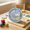 A wooden Montessori busy board for toddlers featuring colorful gears, switches, and sensory elements on a light wood surface.