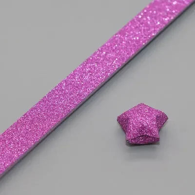 A pink glitter paper strip is shown alongside a formed pink glitter origami star.