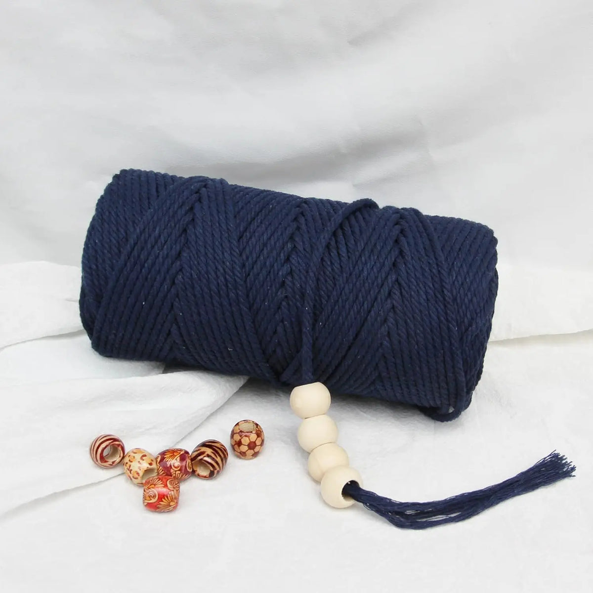 A dark navy blue macrame rope coiled and with wooden beads extending from it on a white background.