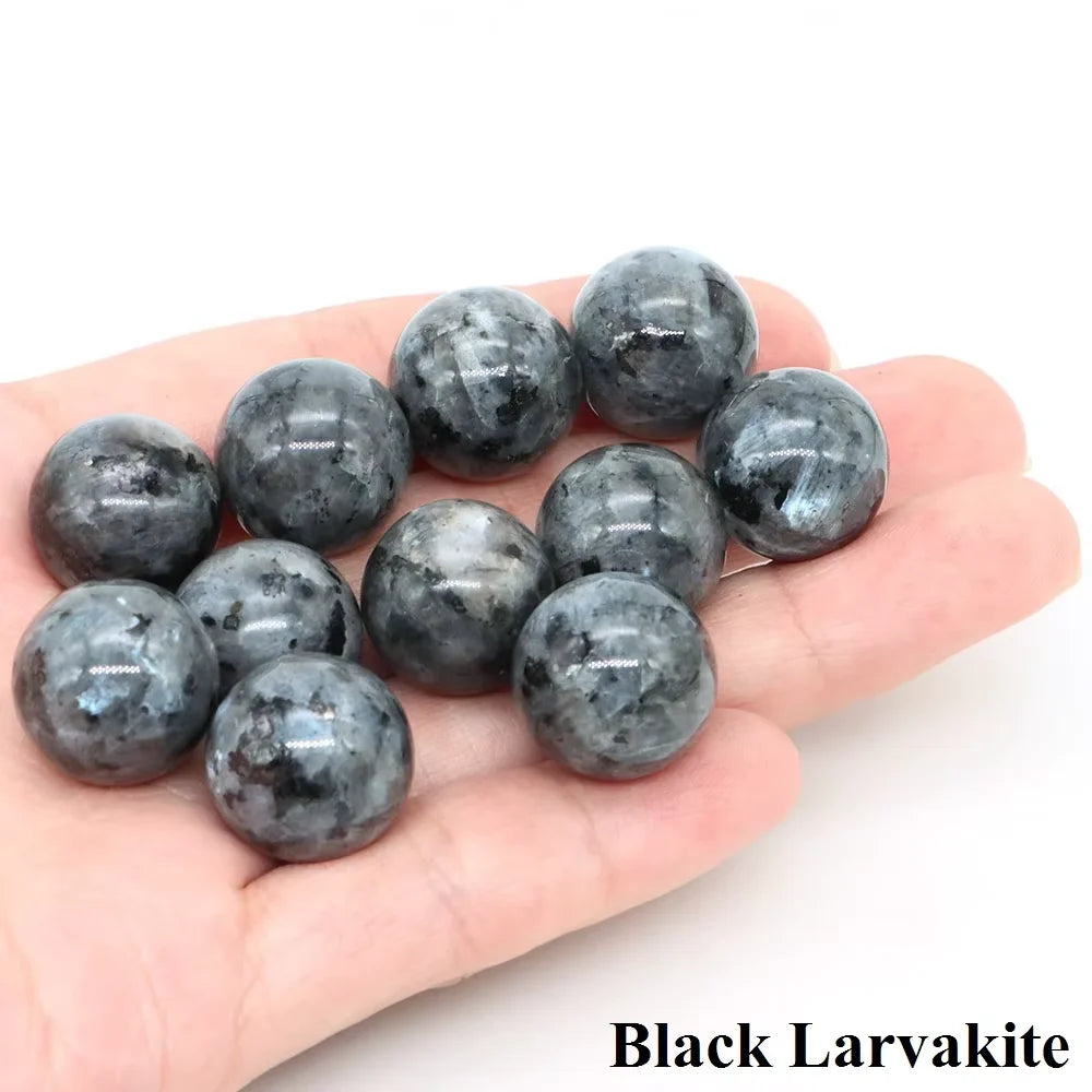 A hand holds several polished black larvakite crystal spheres.