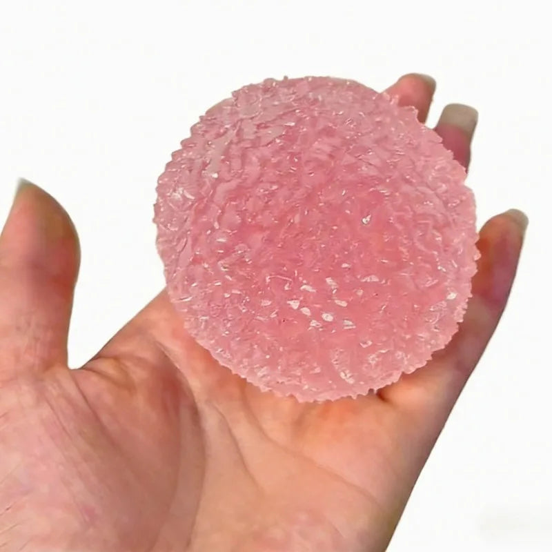 A hand holds a pink squishy ice ball mochi fidget toy with a textured surface.