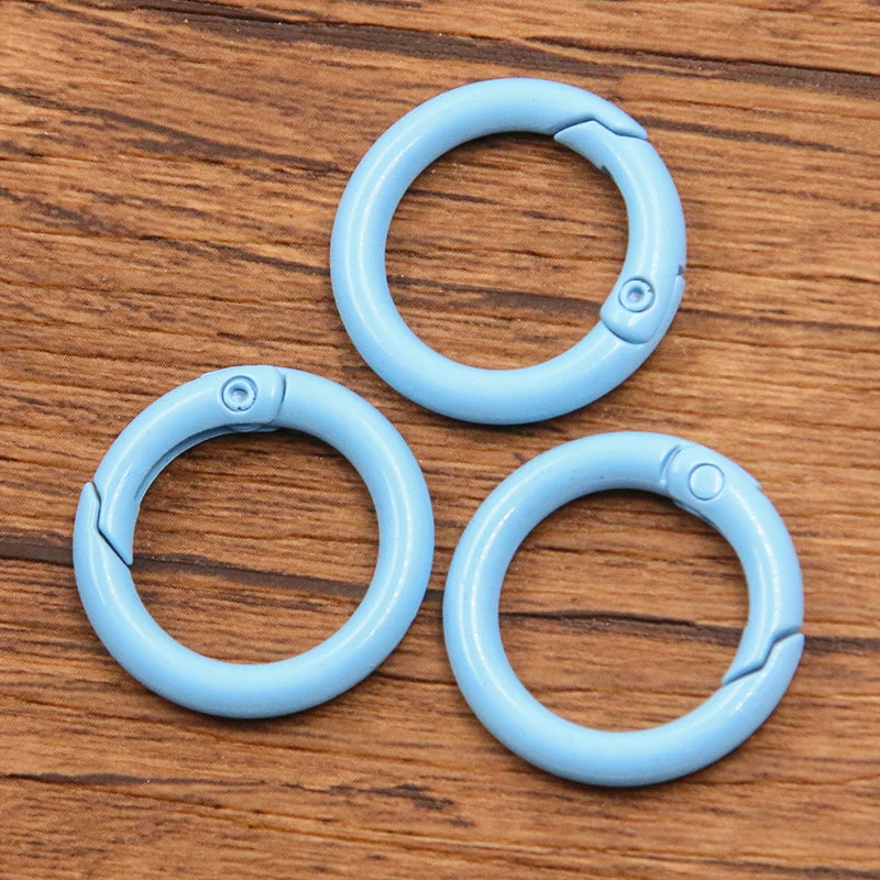 A set of ten light blue metal O-ring spring clasps arranged in a cluster on a wooden surface.
