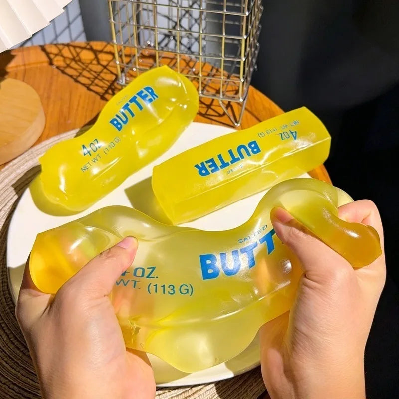 A hand holds a yellow moldable butter stick squishy stress relief fidget toy on a white plate.
