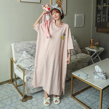 A woman wearing a pink and white striped short-sleeve lounge dress with a cat-ear headband sits on a sofa.
