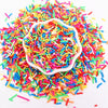 A pile of multi-colored polymer clay sprinkles mixed with white sprinkles in a decorative mold.
