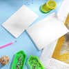 A flat lay showing white double-sided non-stick release paper for diamond painting alongside citrus slices and a pink pen.