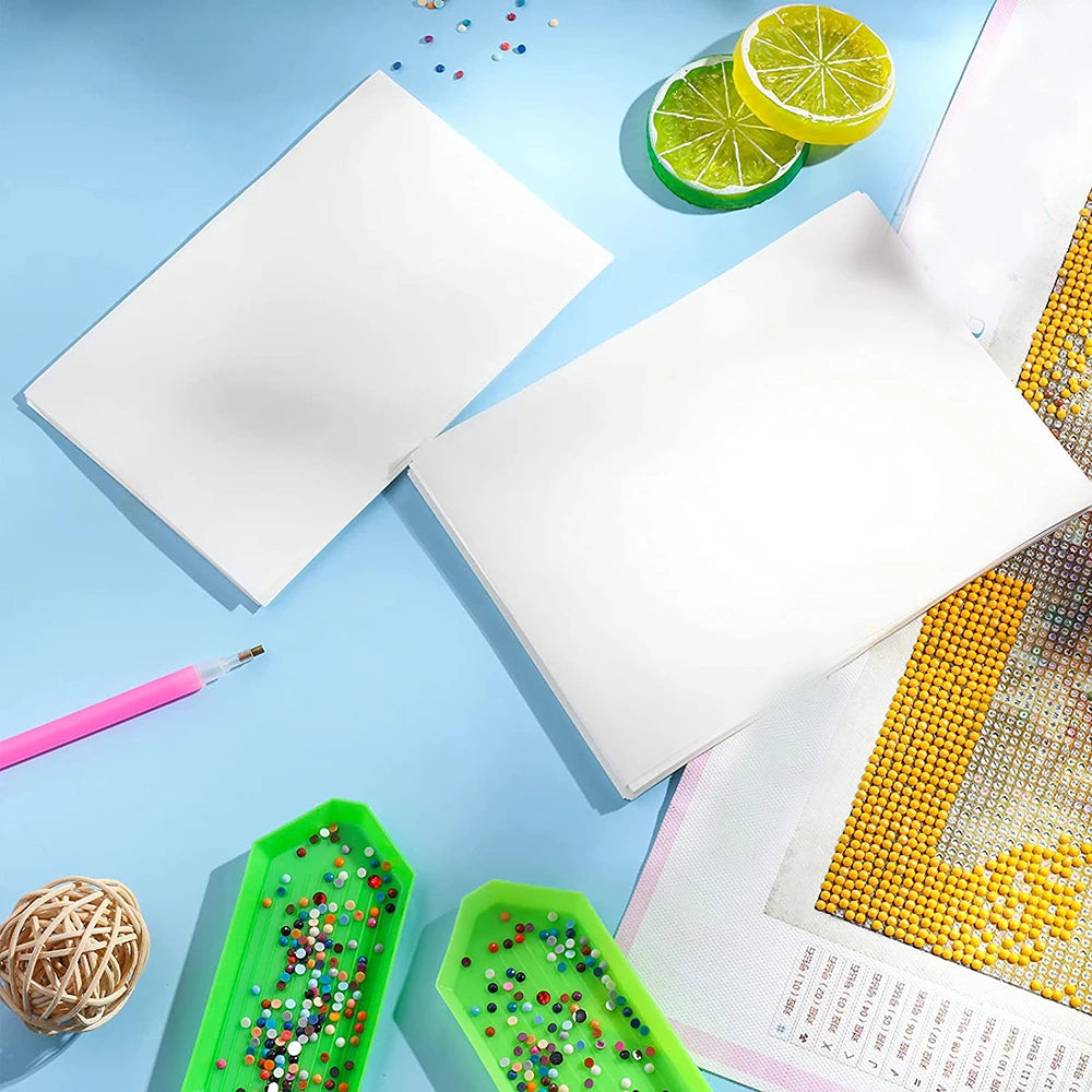 A flat lay showing white double-sided non-stick release paper for diamond painting alongside citrus slices and a pink pen.