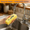A hand is rinsing a yellow butter-shaped squishy under running water in a kitchen sink.