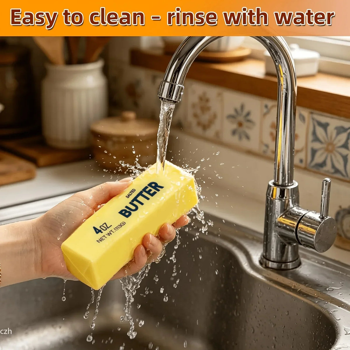 A hand is rinsing a yellow butter-shaped squishy under running water in a kitchen sink.