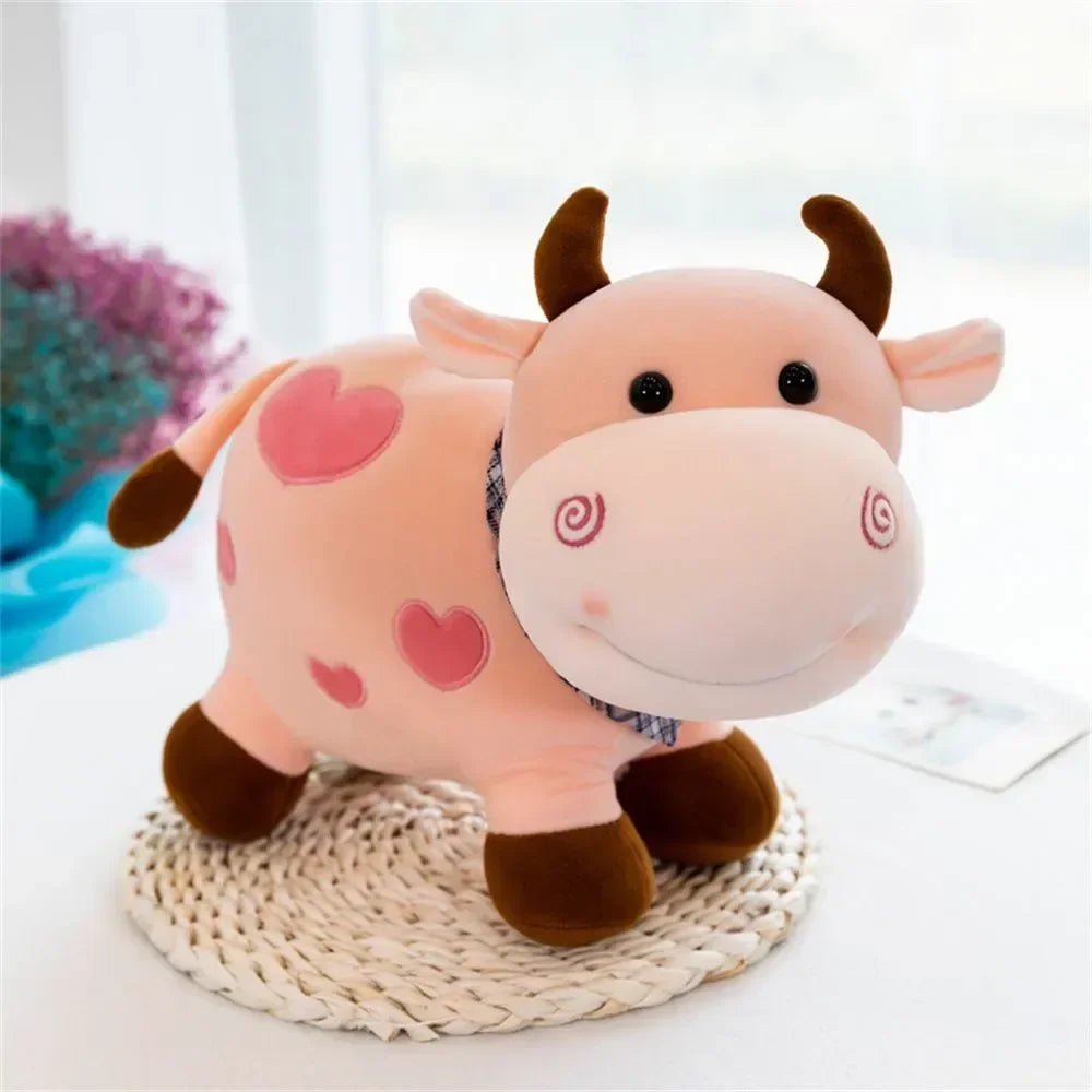 A pink cow plush toy with dark brown accents and heart details sitting on a woven mat.