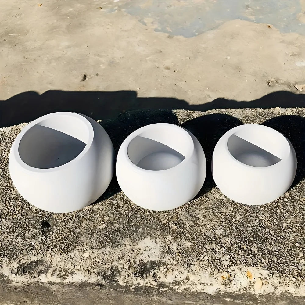 A set of three white silicone round pot molds resting on a rough concrete surface.