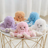A collection of soft, pastel-colored octopus plush toys in purple, orange, blue, pink, and white arranged on a gold wire stan