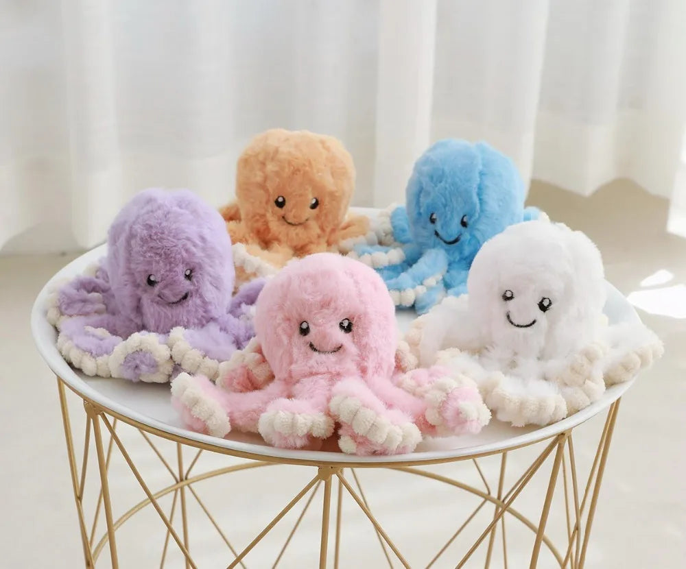 A collection of soft, pastel-colored octopus plush toys in purple, orange, blue, pink, and white arranged on a gold wire stan