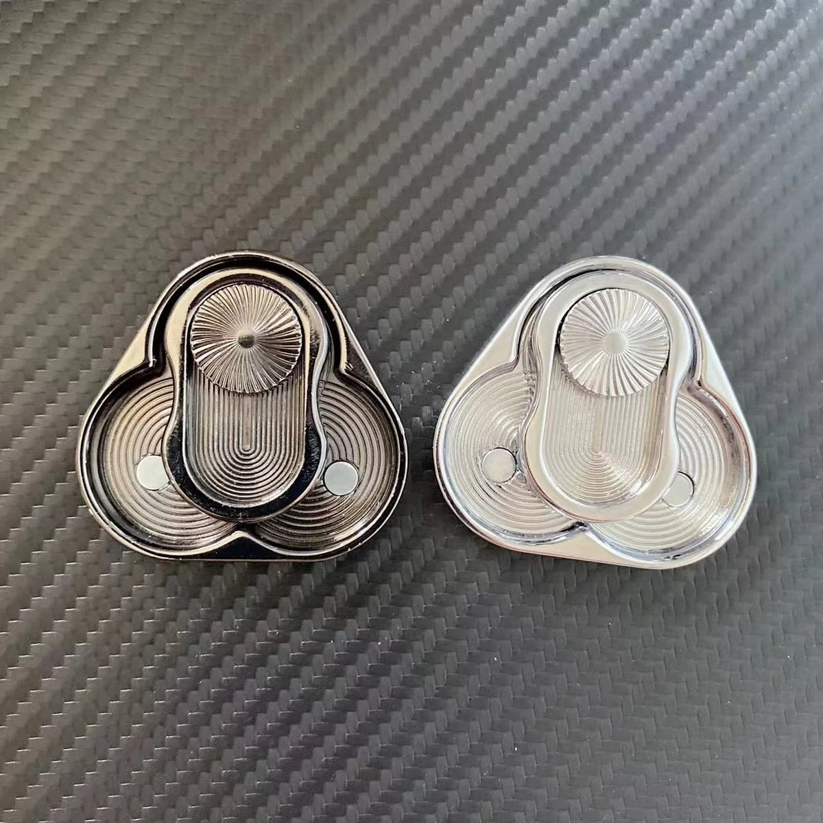 A pair of silver metal magnetic fidget sliders resting on a dark textured surface.