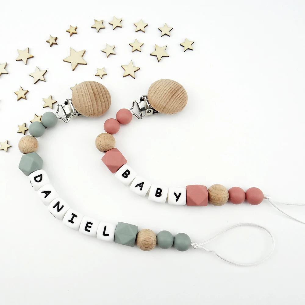 A necklace featuring silicone teething beads and a pacifier clip, with a scattering of wooden stars in the background.