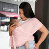 A woman is using an X-shaped baby sling carrier to hold a baby outdoors.