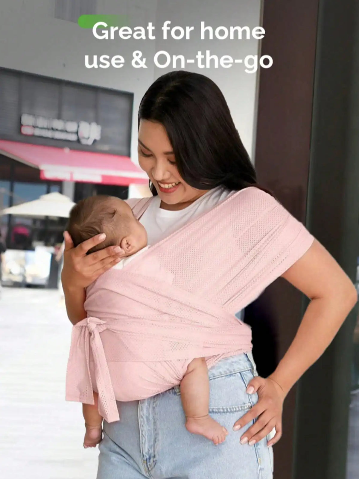 A woman is using an X-shaped baby sling carrier to hold a baby outdoors.