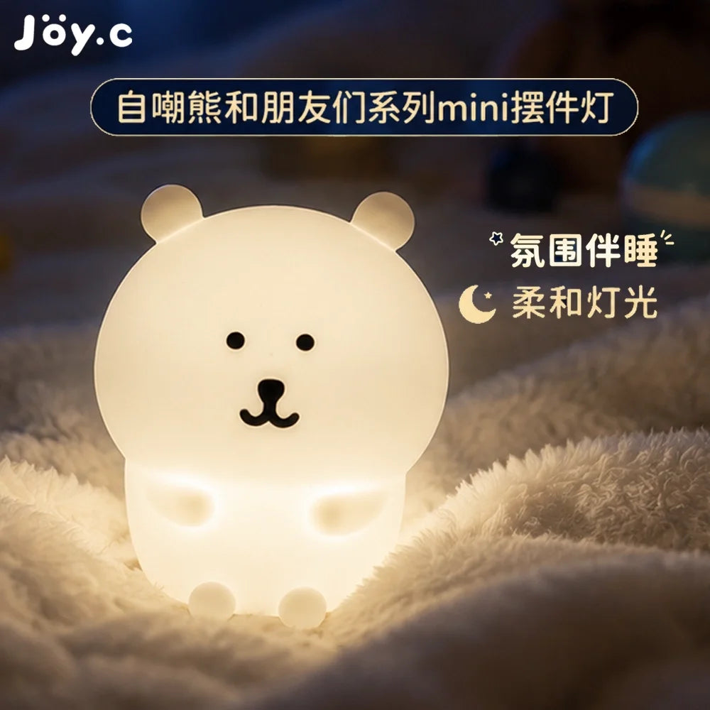 A glowing white bear-shaped silicone night light resting on a fluffy white surface.