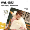 A white plush goose pillow with an orange beak is shown next to a person reading a book.