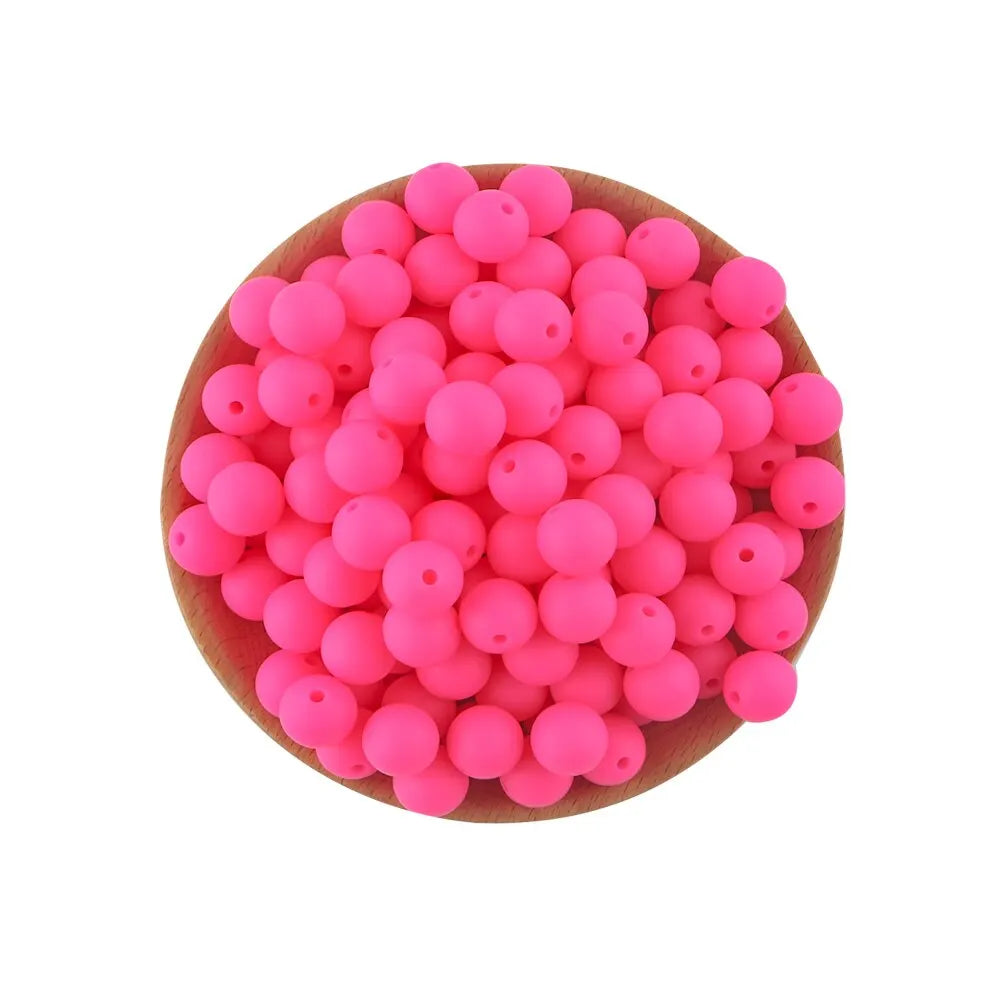 A pile of bright pink silicone round beads for jewelry making and DIY crafts arranged on a wooden surface.
