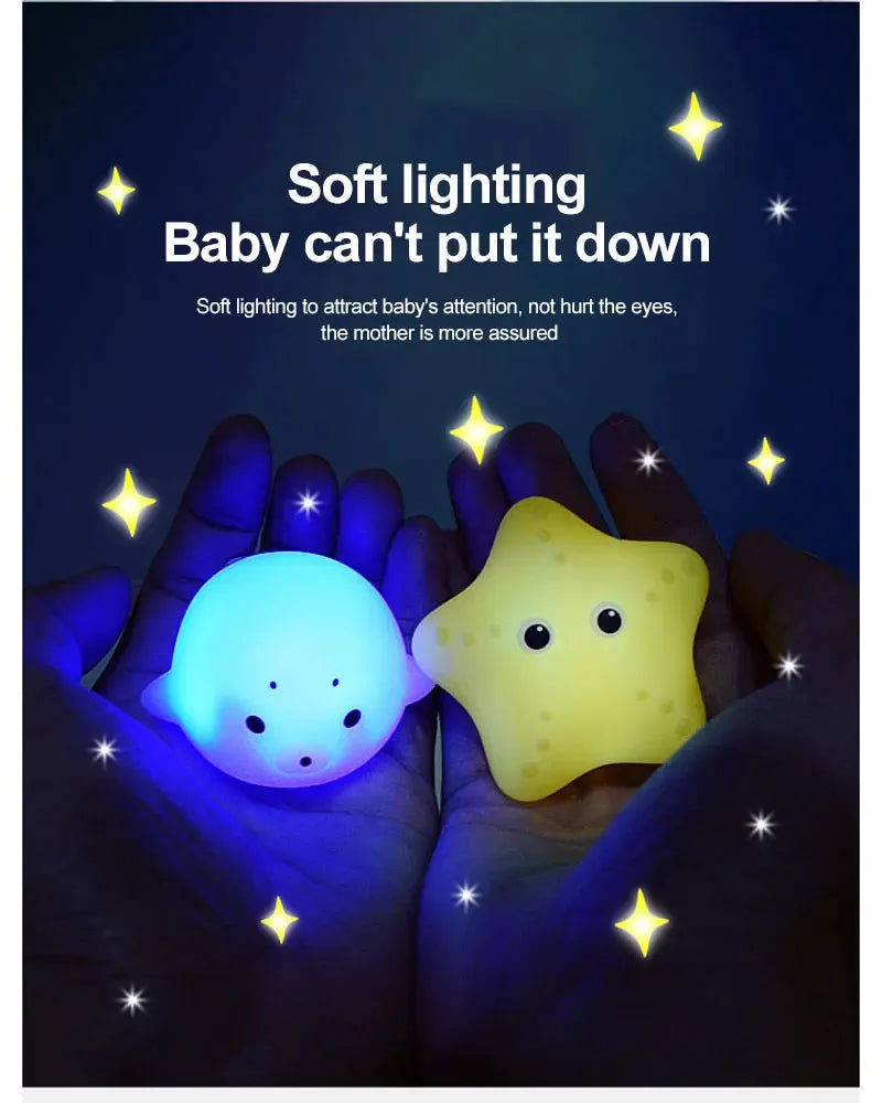 A pair of hands holds a glowing yellow light-up toy for babies against a dark background.