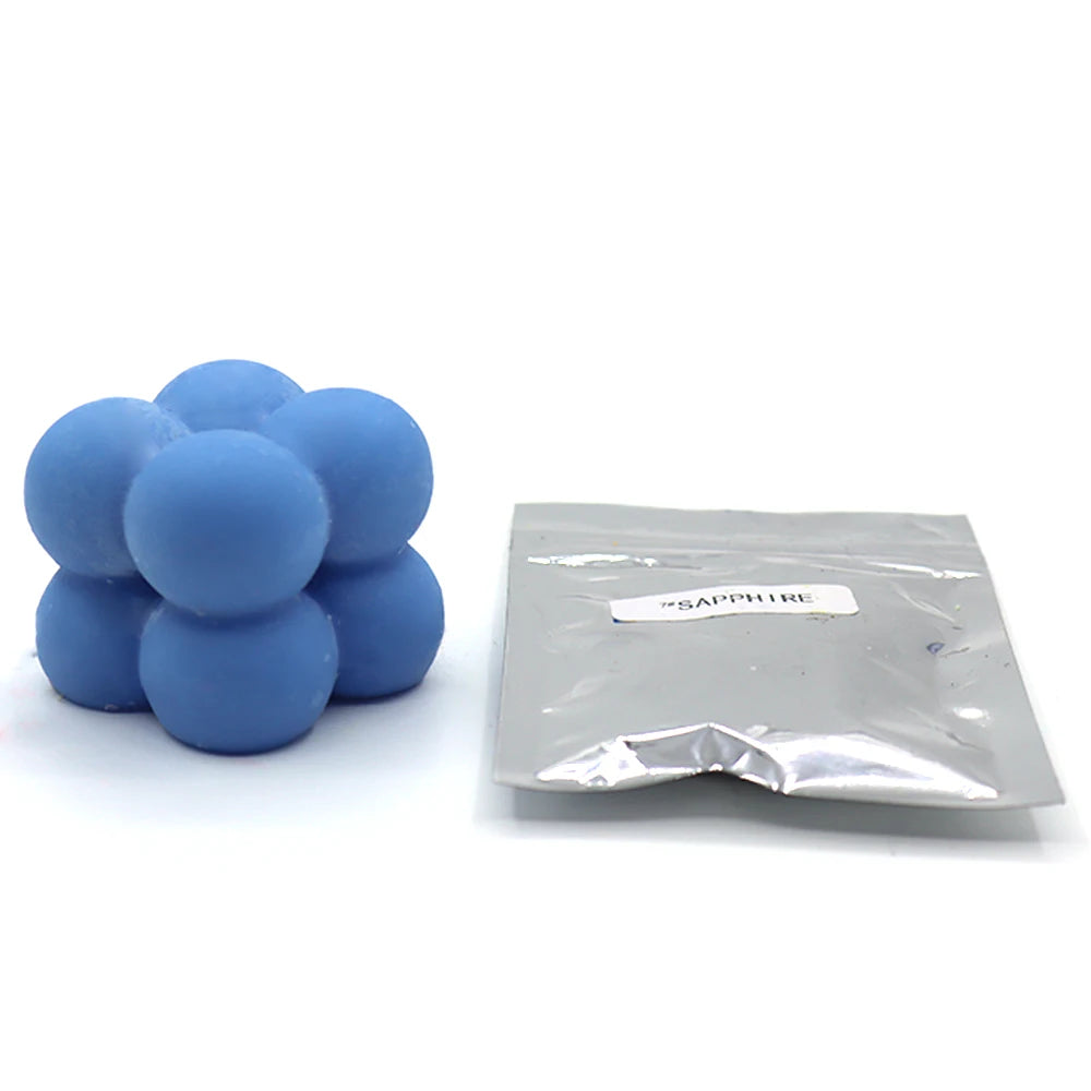 A pile of light blue candle dye chips next to a small plastic bag labeled Sapphire