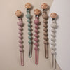 A collection of silicone pacifier clips featuring bear paw shapes in pink, green, and beige tones.