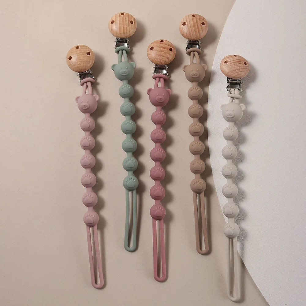 A collection of silicone pacifier clips featuring bear paw shapes in pink, green, and beige tones.