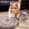 A fluffy orange cat is interacting with a motion-activated toy that features a rolling ball and hide elements.