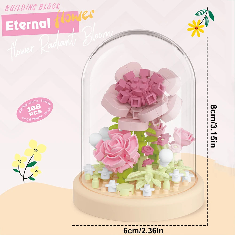 A clear glass dome displays a pink flower bouquet made from building blocks, featuring various shades of pink and green.