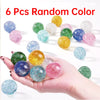 A hand holds six random colored glitter bouncy balls on a white background.