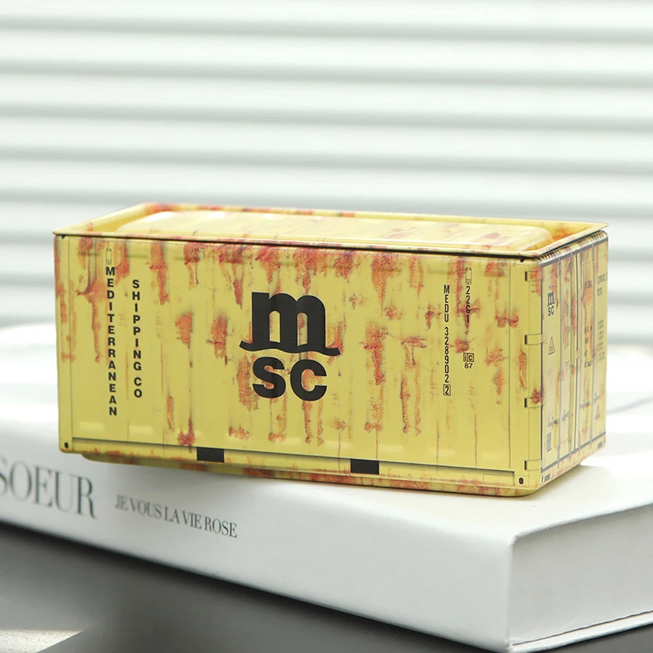 A rectangular yellow storage box with a lid and textured surface is shown resting on a white book.