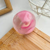 A translucent pink squishy stress ball with a visible slice of fruit inside, resting on a wooden cutting board.