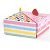 A pink and multicolored gift box with a lid open, featuring a candle and dot-shaped paper decorations.