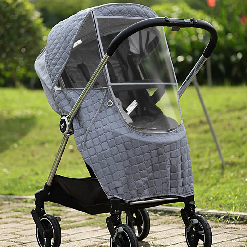 A gray universal waterproof winter stroller cover with a clear window and a black frame is shown outdoors.