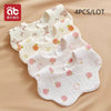 A set of four white cotton gauze baby bibs with various floral and fruit patterns laid out on a beige background.