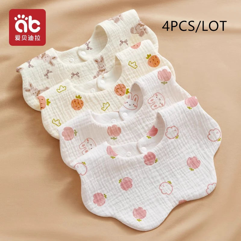 A set of four white cotton gauze baby bibs with various floral and fruit patterns laid out on a beige background.