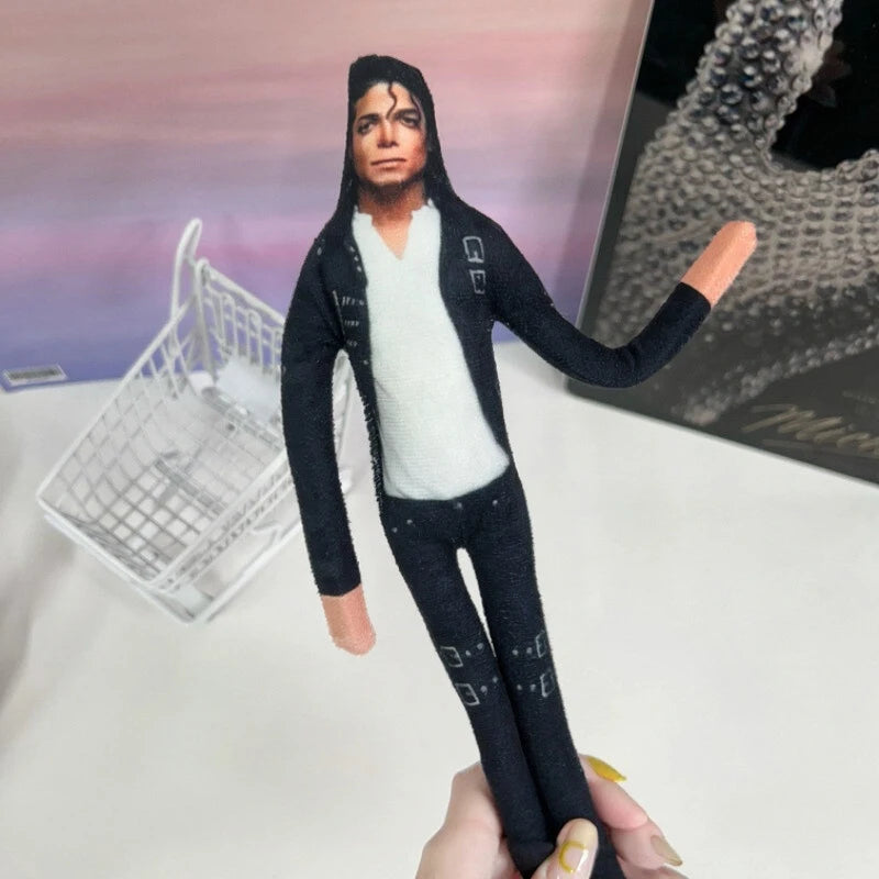 A collectible plush doll of Michael Jackson with movable joints, dressed in a black outfit and white shirt.