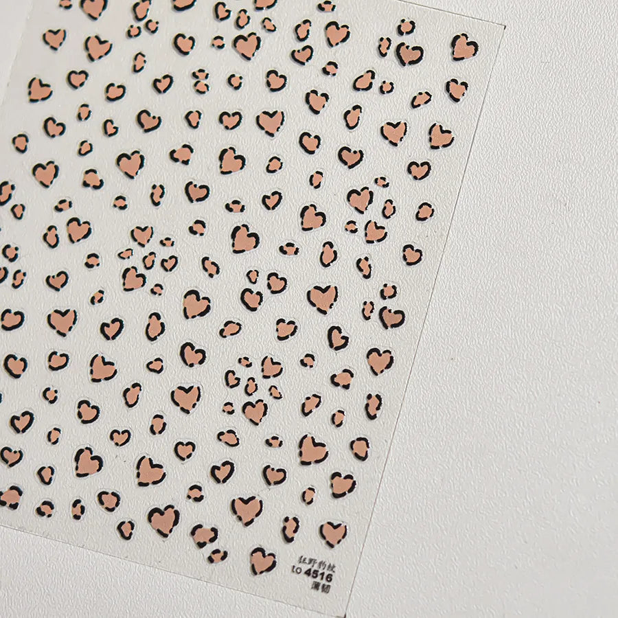 A sheet of nail art stickers featuring small, irregular heart shapes in a nude and gold leopard print pattern.