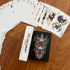 A black and white poker card deck featuring Hollow Knight themed cards resting on a wooden surface.
