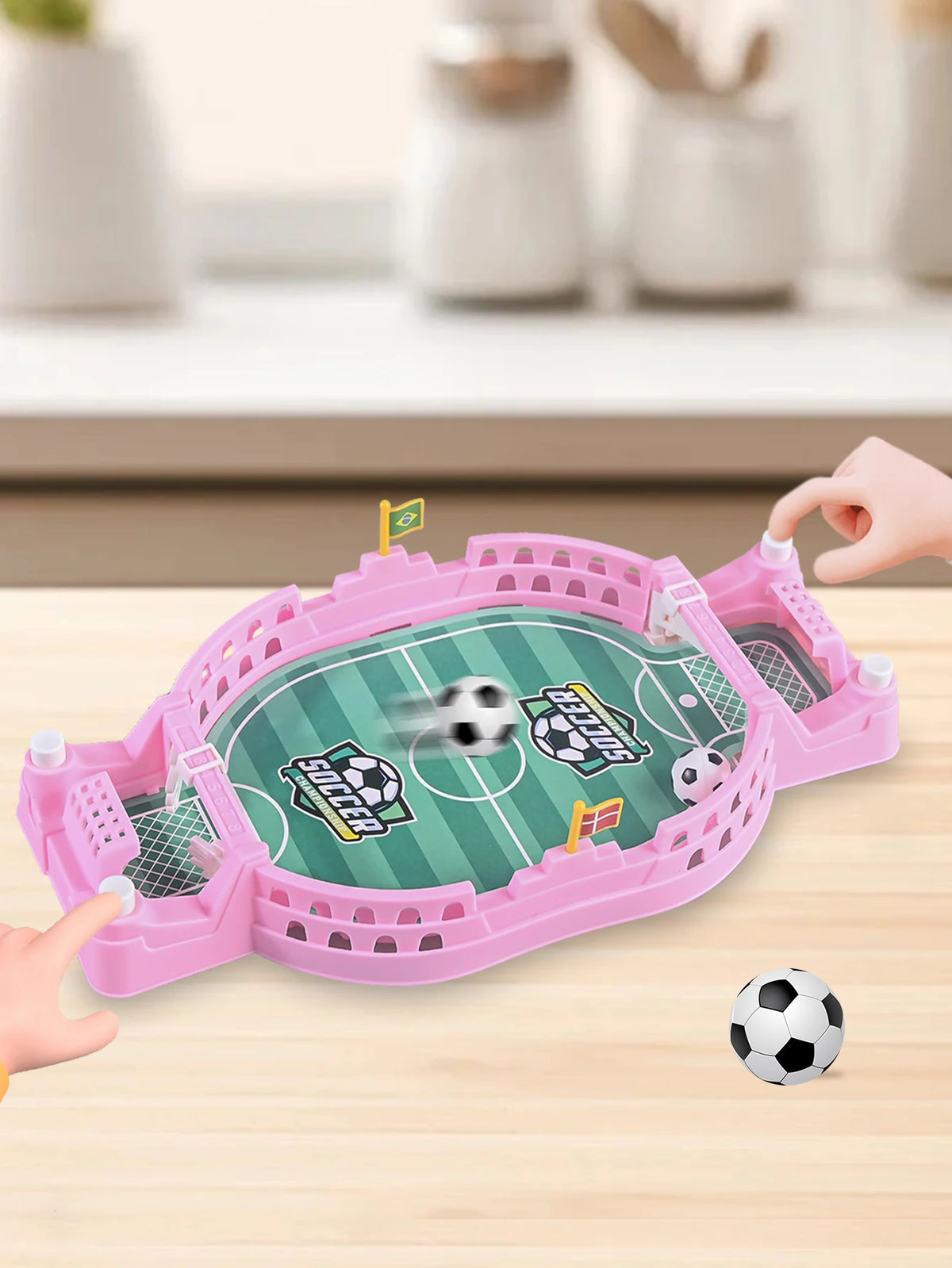 A pink tabletop foosball game with a green field and soccer ball is being played on a wooden table.