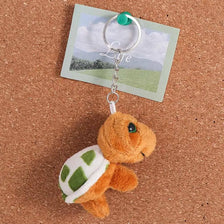 An adorable orange turtle plush toy attached to a silver keyring with a green loop and a white card.
